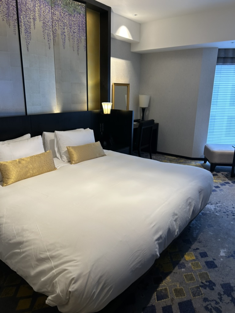THE HOTEL SANRAKU KANAZAWAの客室。屏風モチーフのヘッドボードと金色のクッションが置かれた広々としたベッド