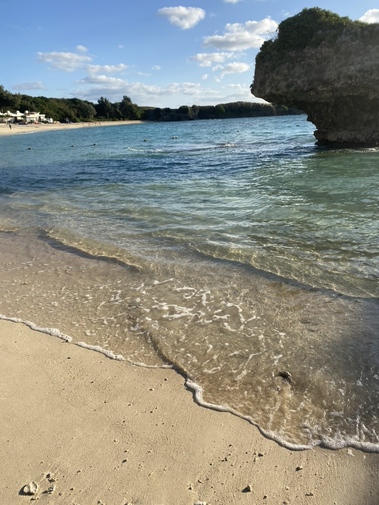 ニライビーチの波打ち際。透き通ったアリビラブルーの海と大きな岩